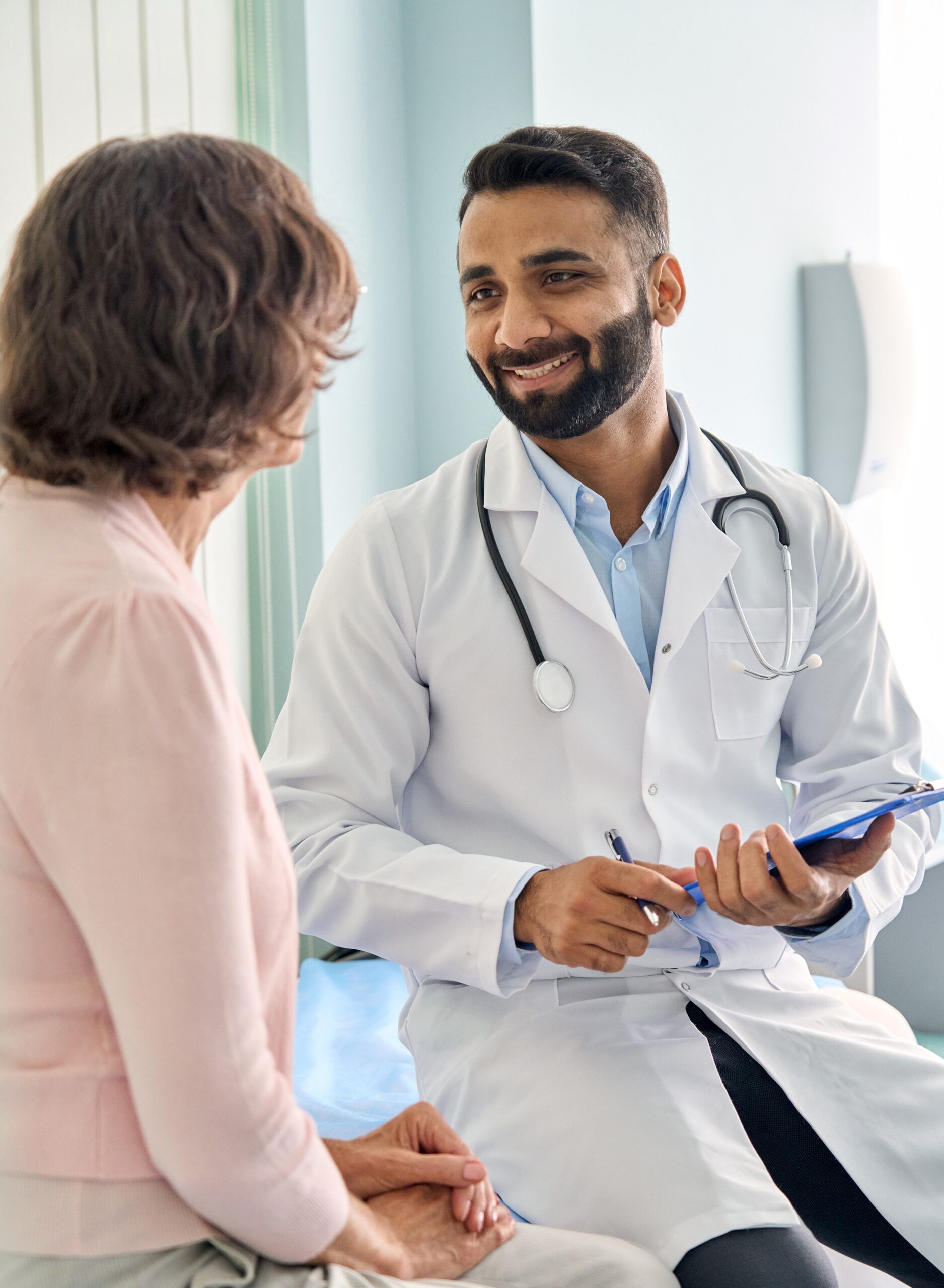 Happy Indian doctor consulting female older patient in hospital Vertical - Peak Health