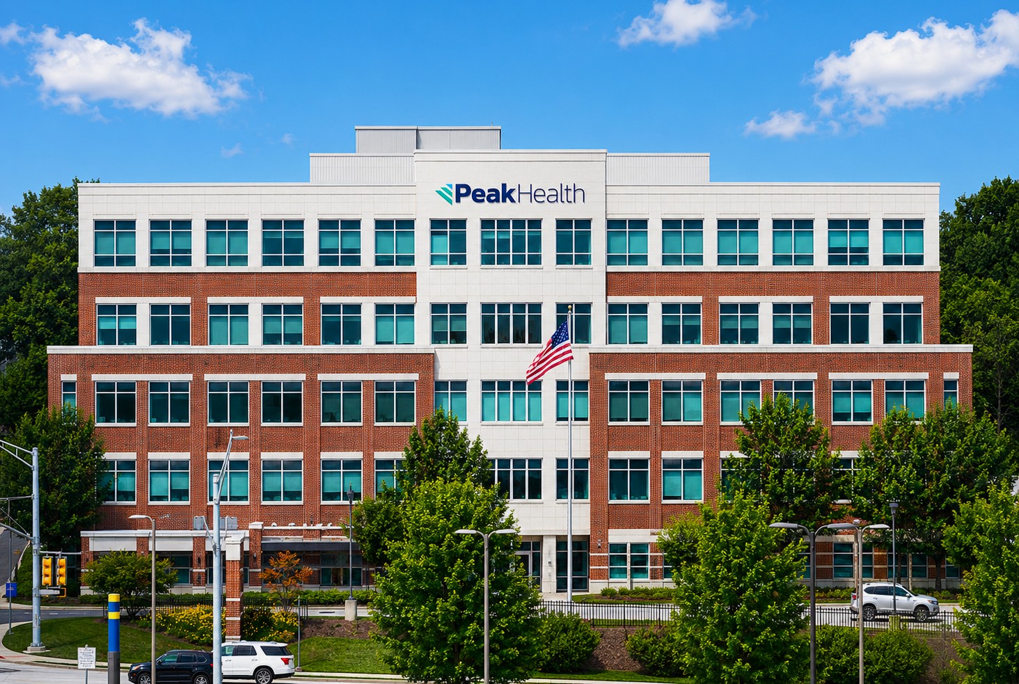 Modern multi-story Peak Health building with red brick and white facade, blue-tinted windows, and a central flagpole with the American flag.
